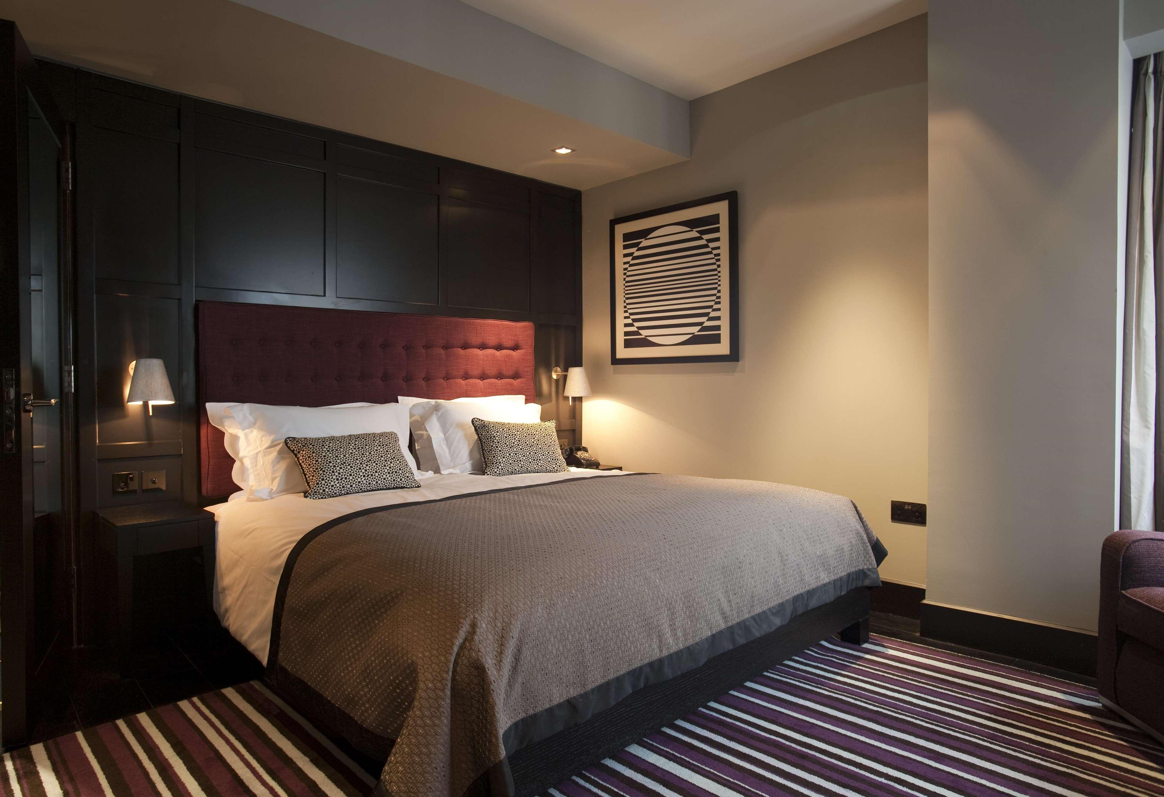 The Fitzwilliam Hotel Белфаст Екстер'єр фото The photo shows a stylish and modern hotel room. It features a large bed with a tufted headboard in a deep burgundy color. The bed is dressed with neutral-toned bedding and decorative pillows. On either side of the bed, there are small bedside lamps 