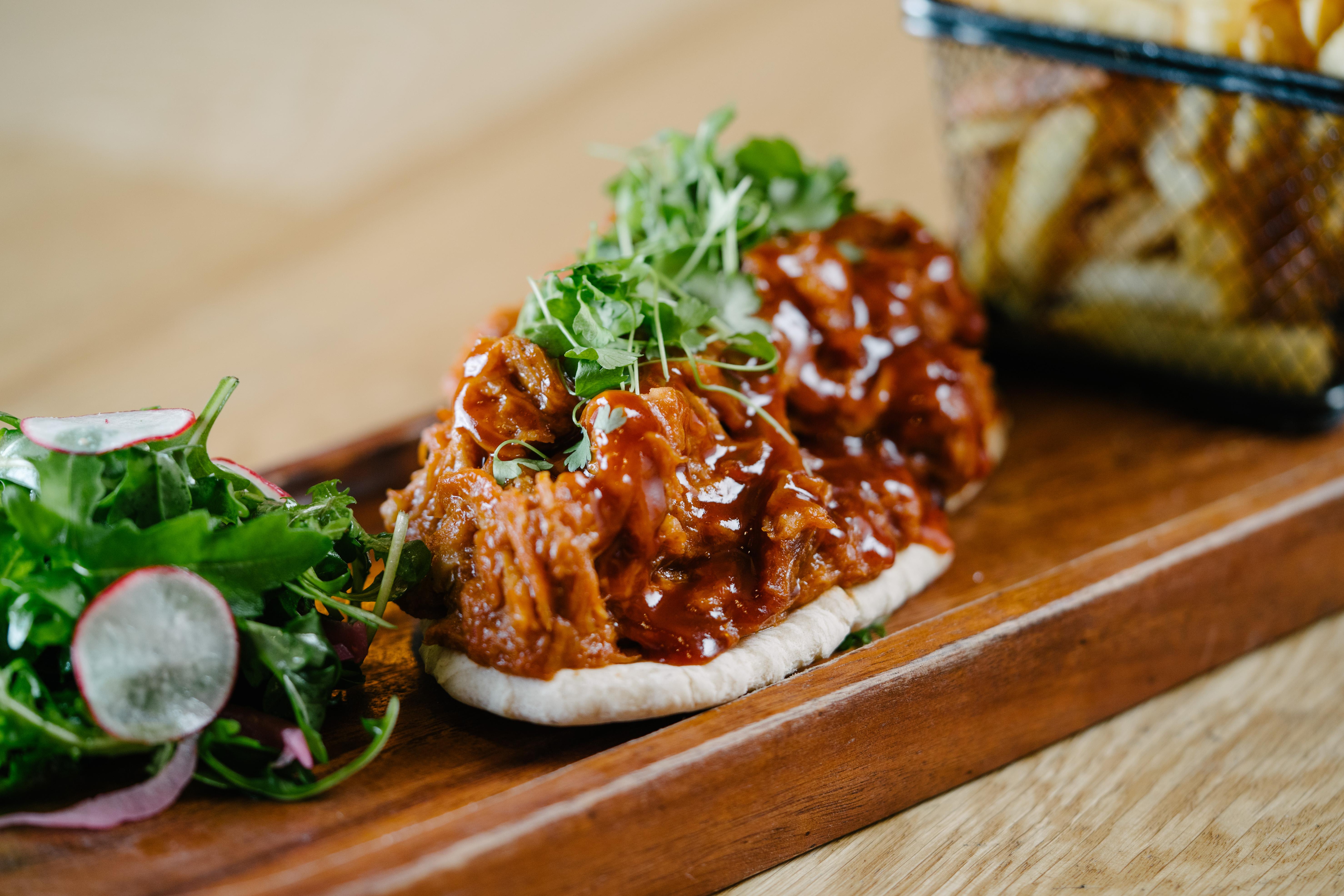The Fitzwilliam Hotel Белфаст Екстер'єр фото The photo shows a wooden platter featuring two pieces of bread topped with pulled meat covered in a rich barbecue sauce. The dish is garnished with fresh greens, including sprouts. On the side, there is a small serving of mixed salad with radishes an
